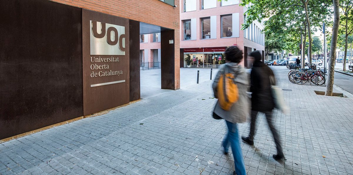 Two people walking towards a building with the UOC logo on it