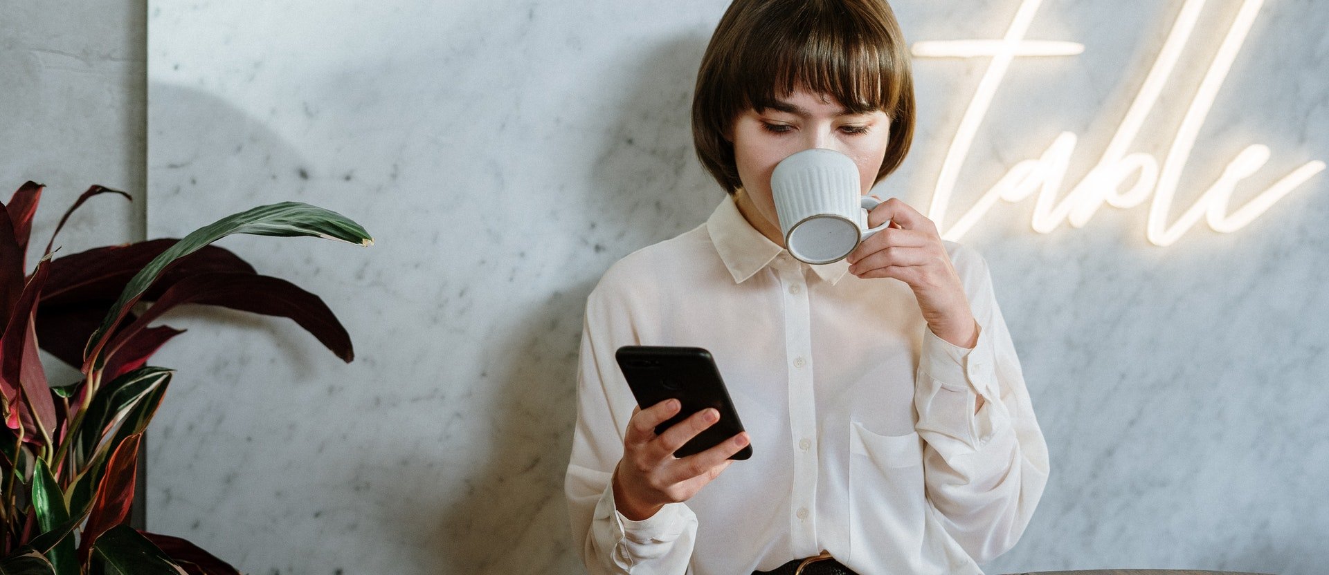 Dona bebent un cafè mentre consulta el mòbil