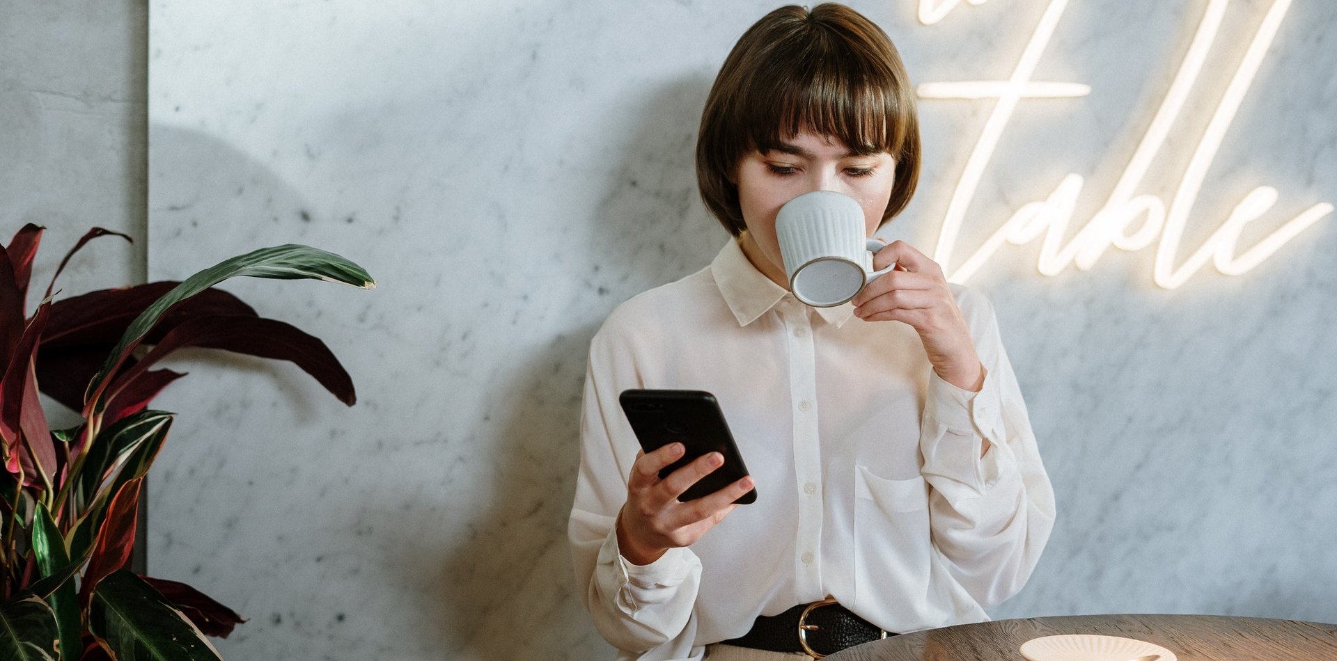 Dona bebent un cafè mentre consulta el mòbil