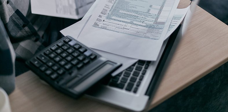 Una calculadora, un portàtil i un formulari de declaració d'impostos a sobre d'una taula