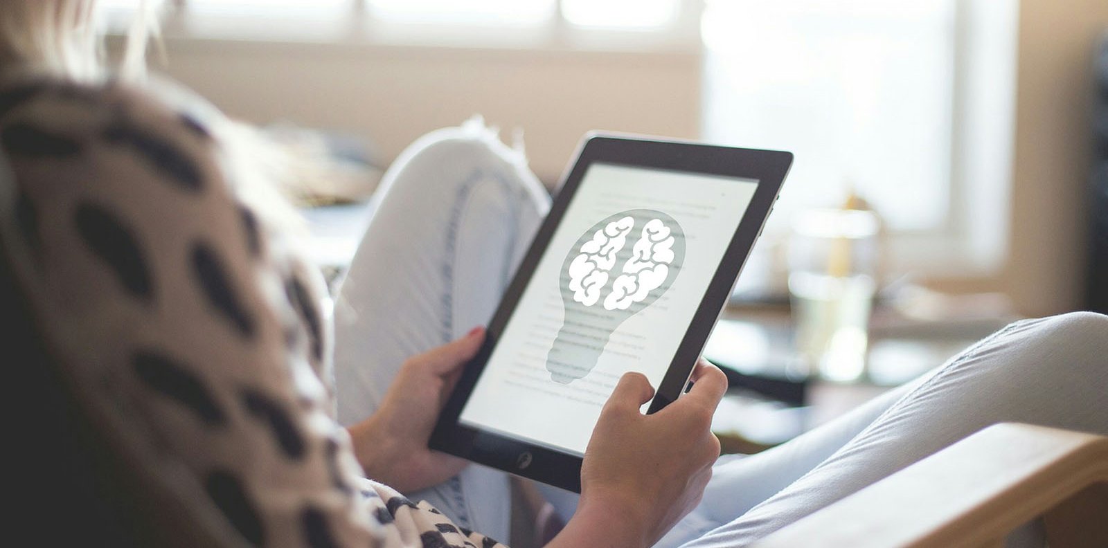 A person with an ebook reading a text accompanied by a representation of a brain