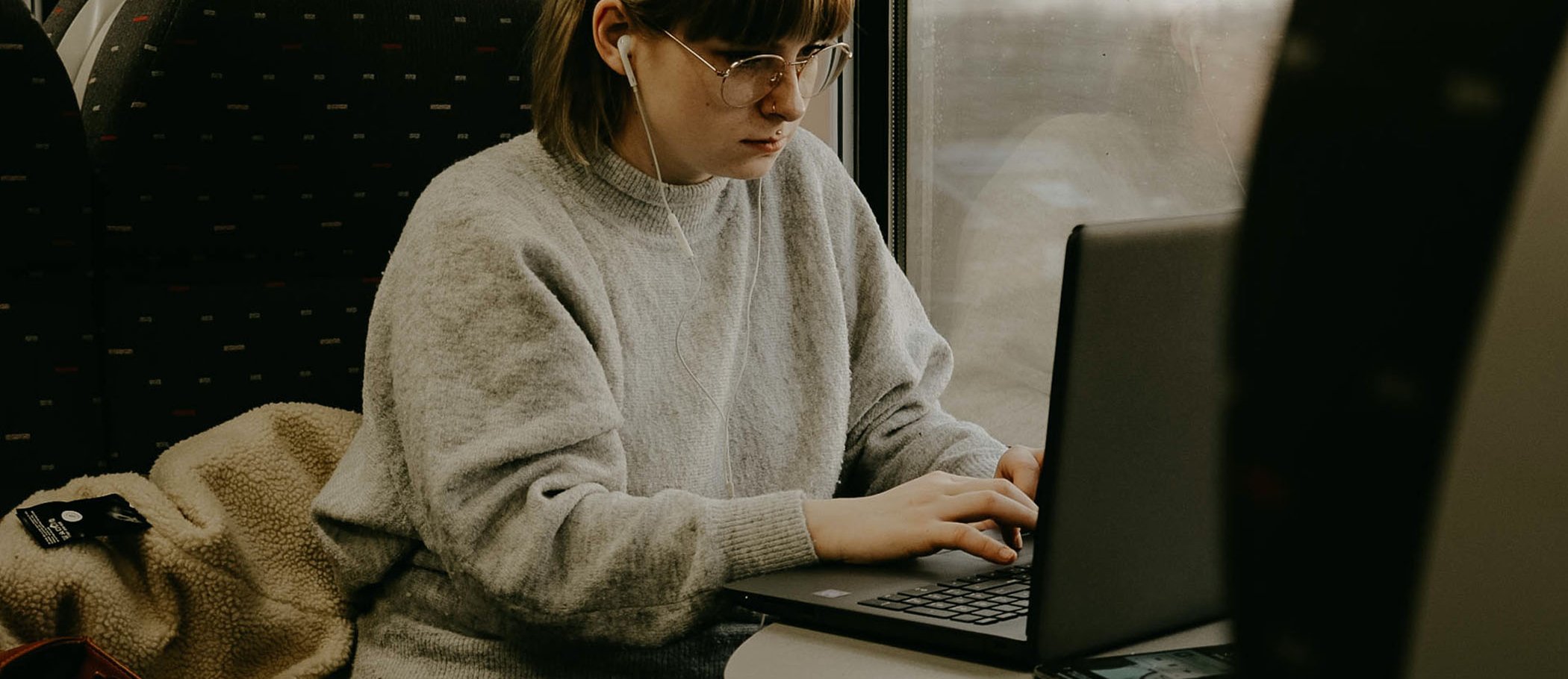 Una noia asseguda en un tren, amb auriculars i escrivint en un portàtil
