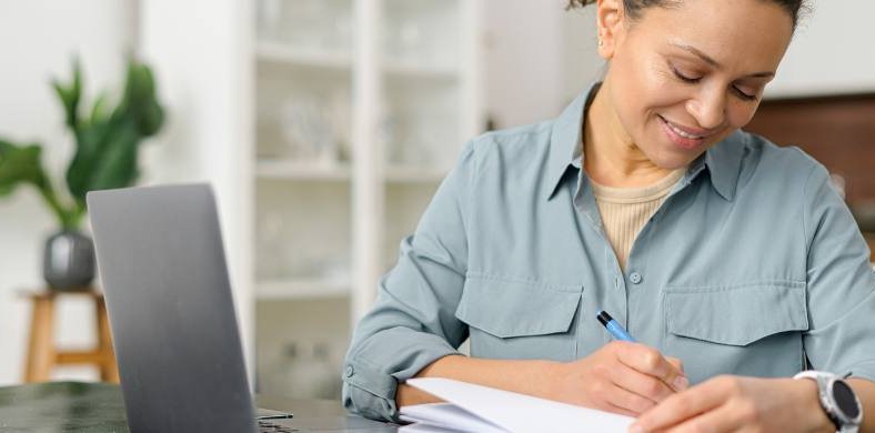 Una dona apuntant en una llibreta mentre fa servir un ordinador