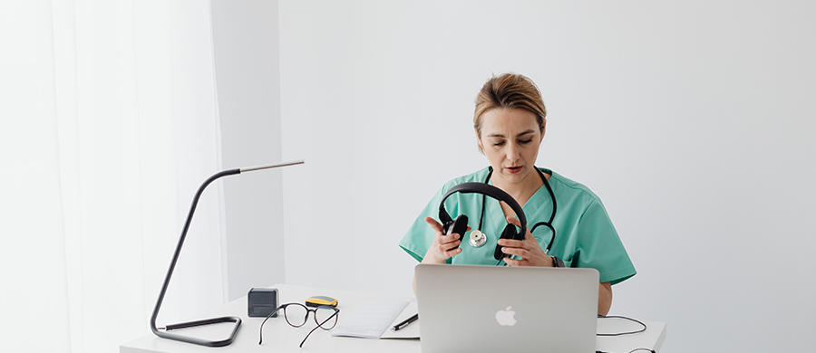 Una médica con un portátil, auriculares y una libreta