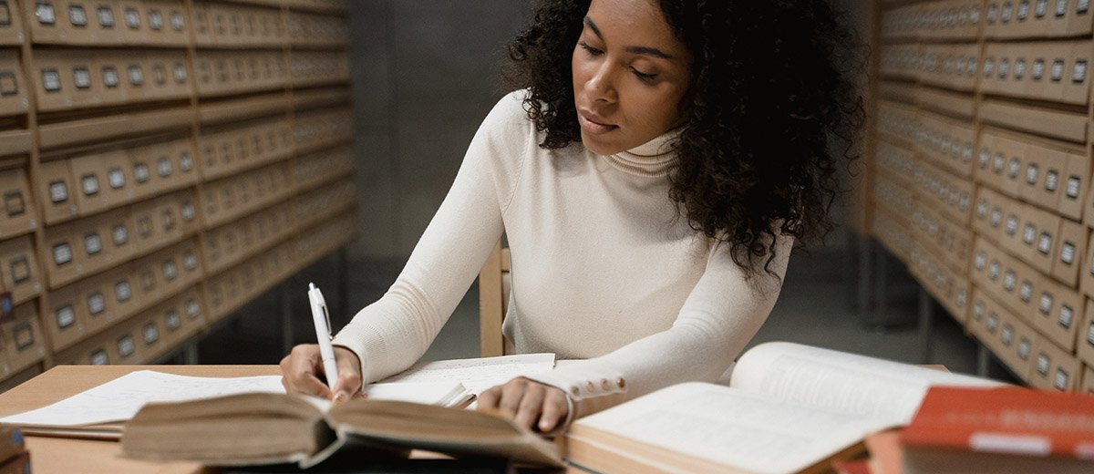 A woman writing at a table full of books