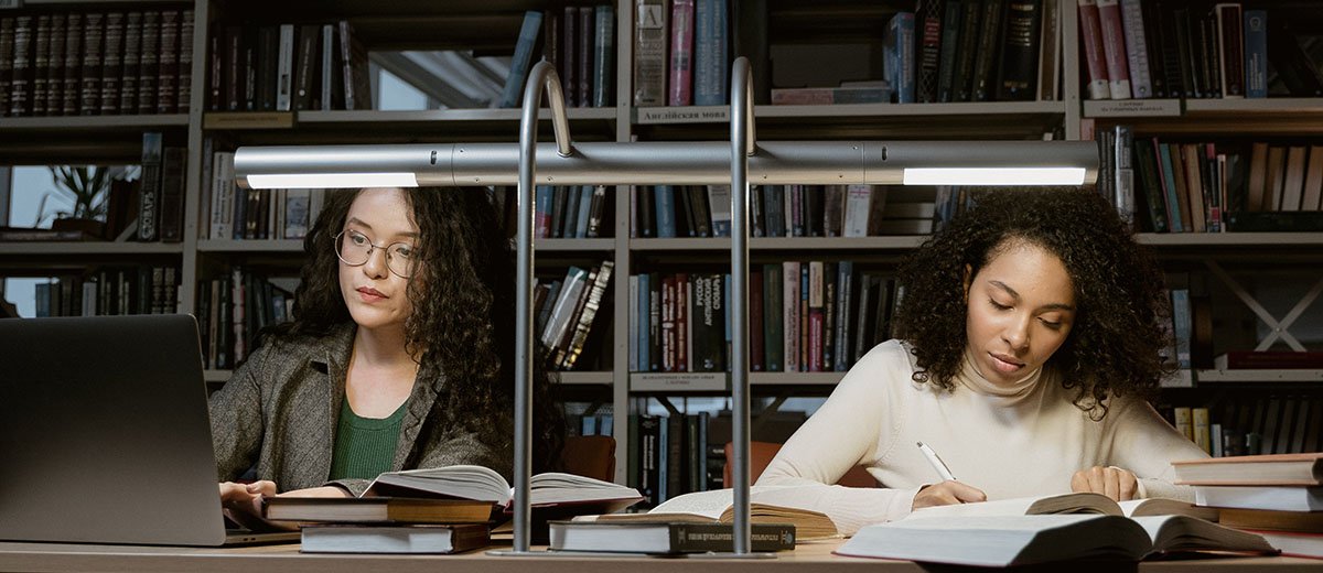 Dos personas trabajando en la mesa de una biblioteca