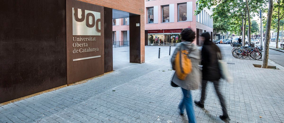 Dos personas caminando hacia un edificio con el logo de la UOC