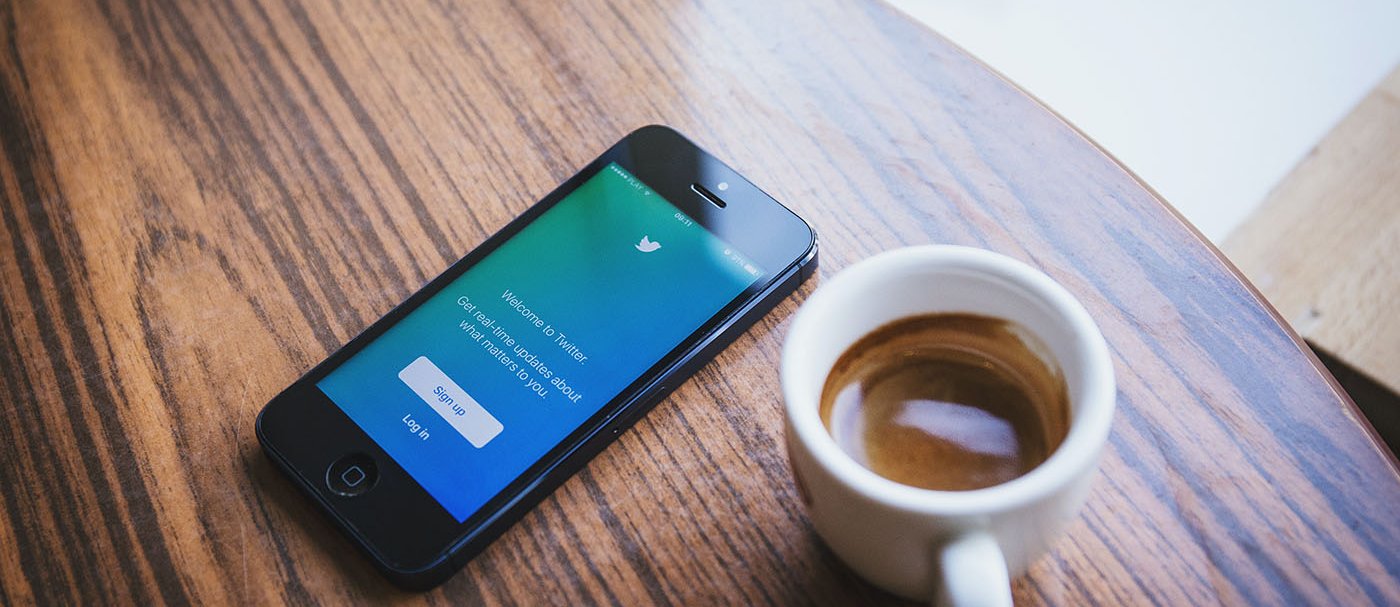 A cup of coffee and a mobile phone with the Twitter login page on the screen.