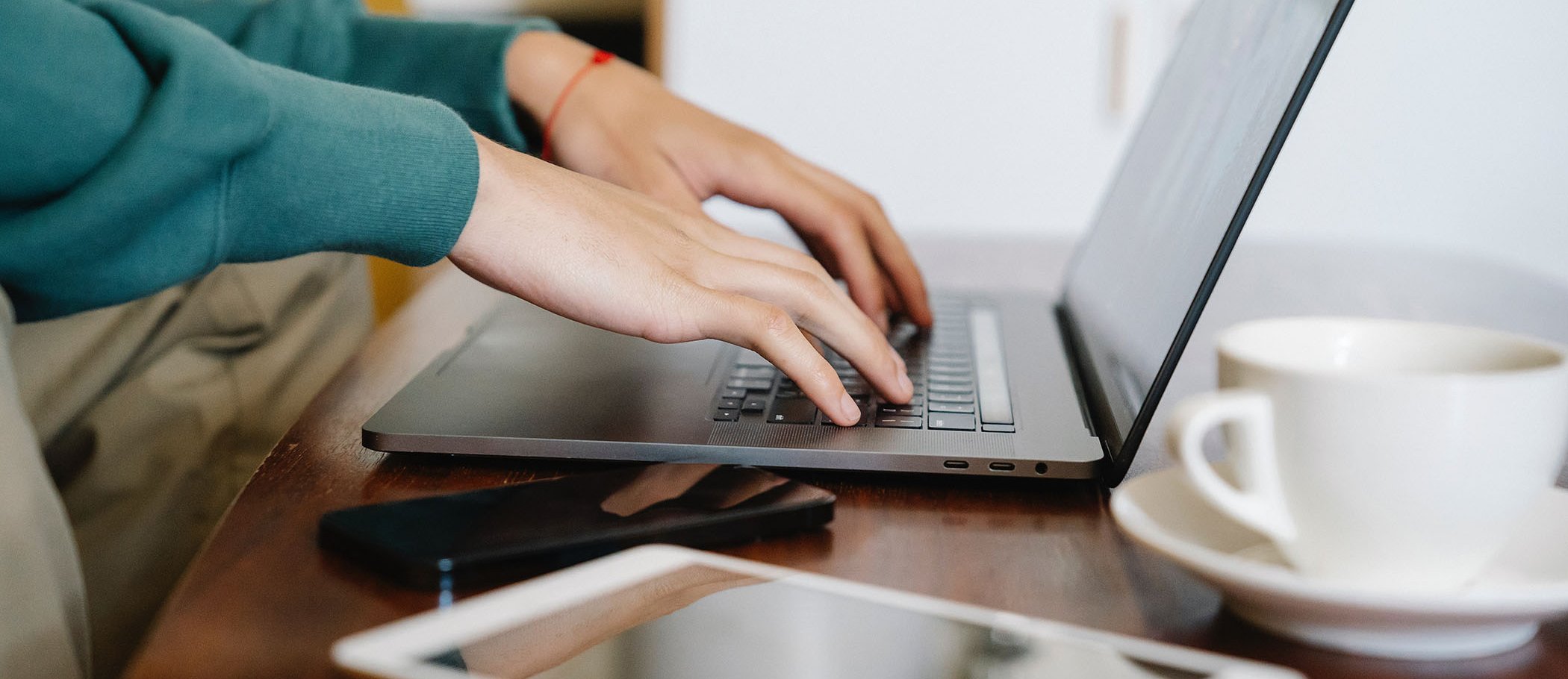 A person using a laptop with a smartphone and a tablet on the table