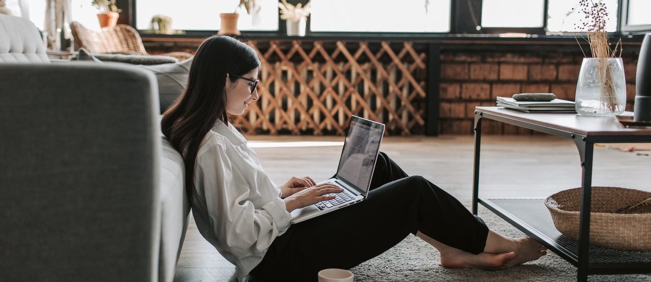 Chica sentada en el suelo con un ordenador portátil encima de las piernas