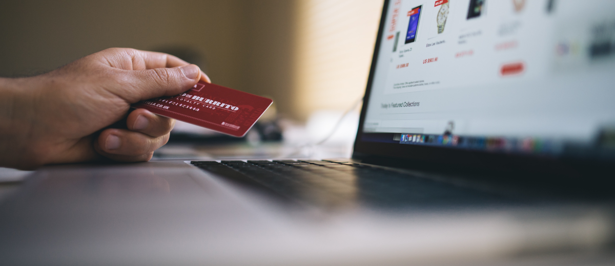 A hand with a credit card and a laptop