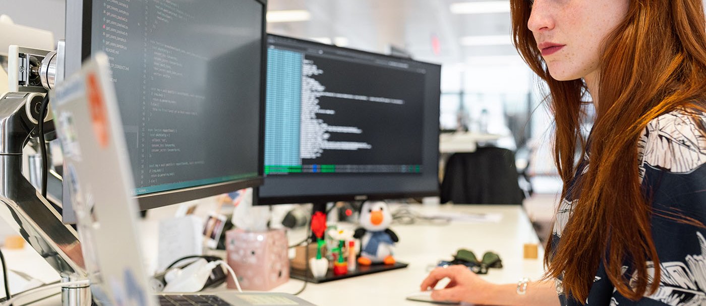 A woman working with three computer screens