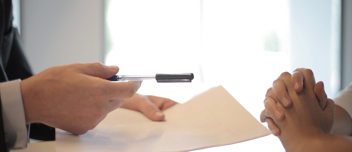 A person offering a pen and a sheet of paper to another person