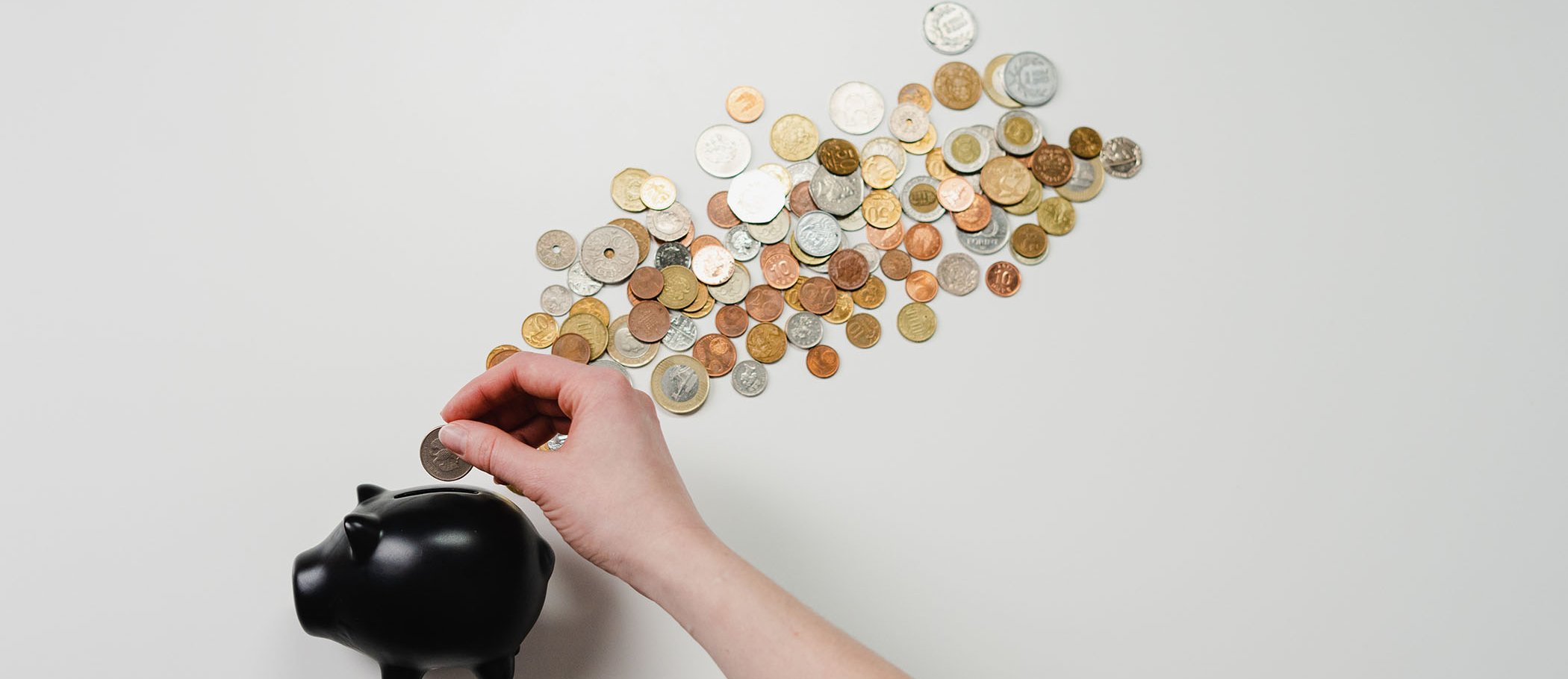 A person putting a coin in a piggy bank, with more coins on the table