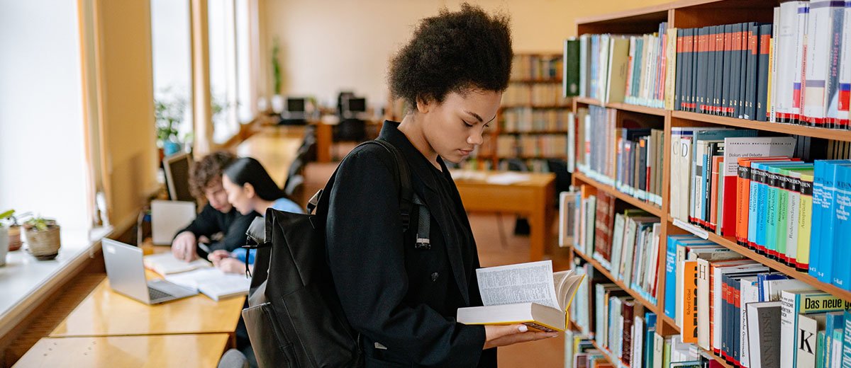 A person taking and browsing a book from a library shelf