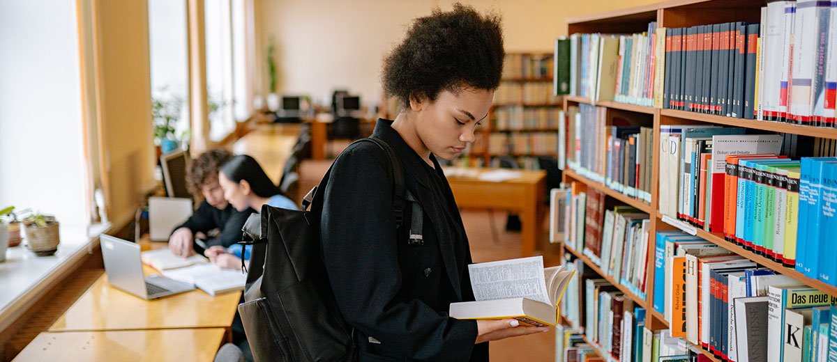 Una persona tomando y hojeando un libro de la estantería de una biblioteca