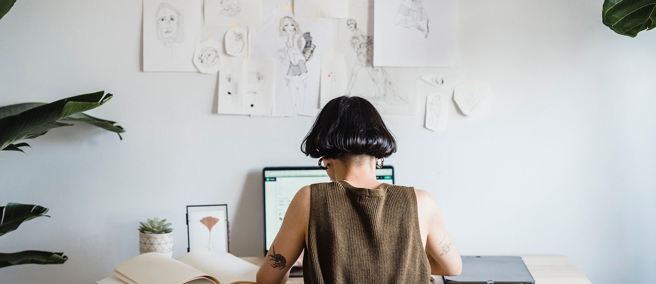 A person using a laptop in front of a wall with several sketches pasted on it