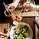 Tres persones estan agafant amb bastonets un menjar japonès anomenat sushi