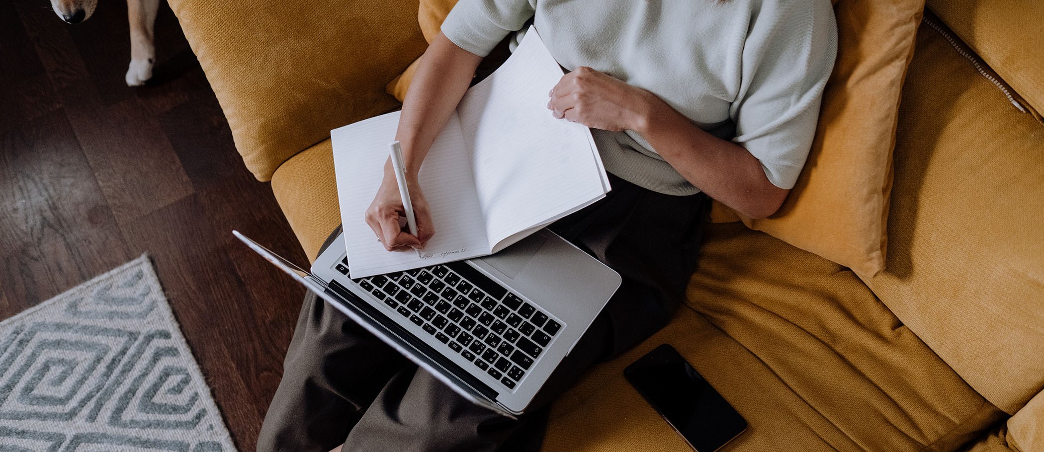 A girl with an open laptop and writing on a notebook 