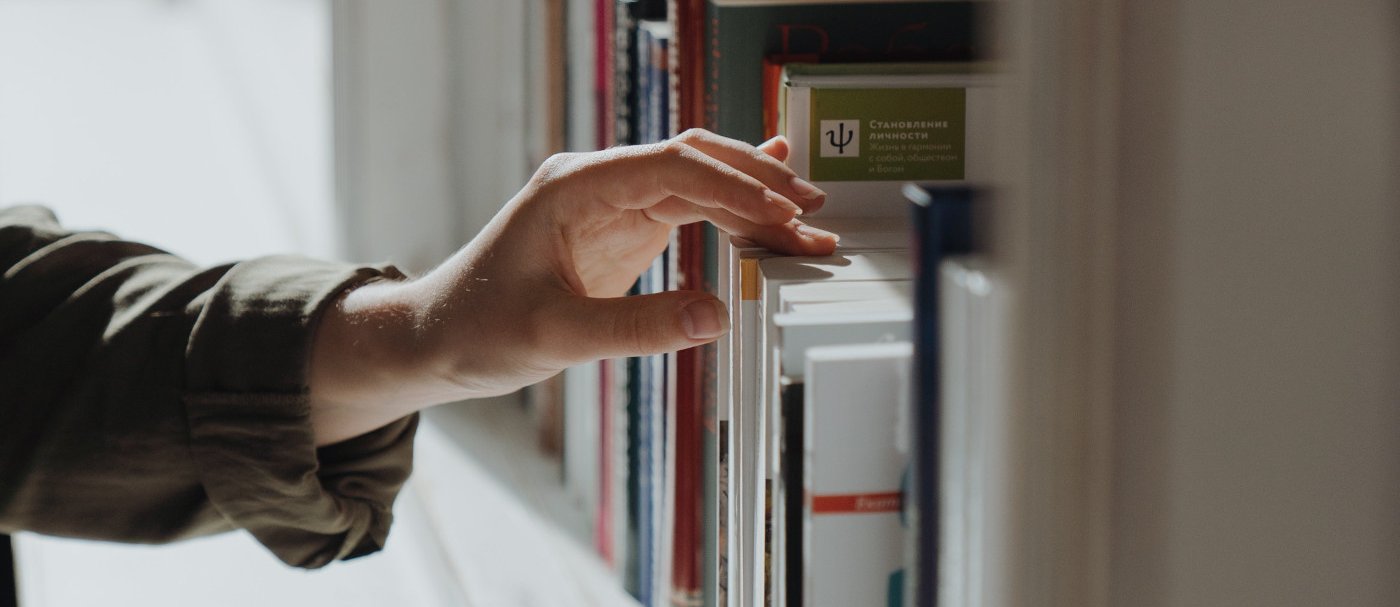 One hand taking a book from a bookshelf