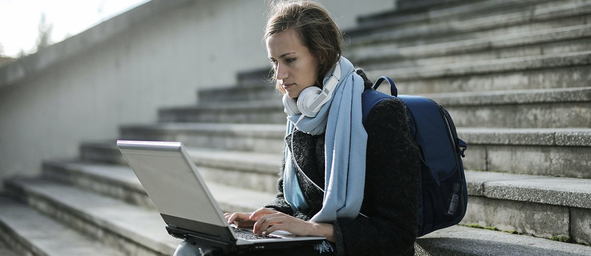 Una chica sentada en unas escaleras escribiendo en un portátil