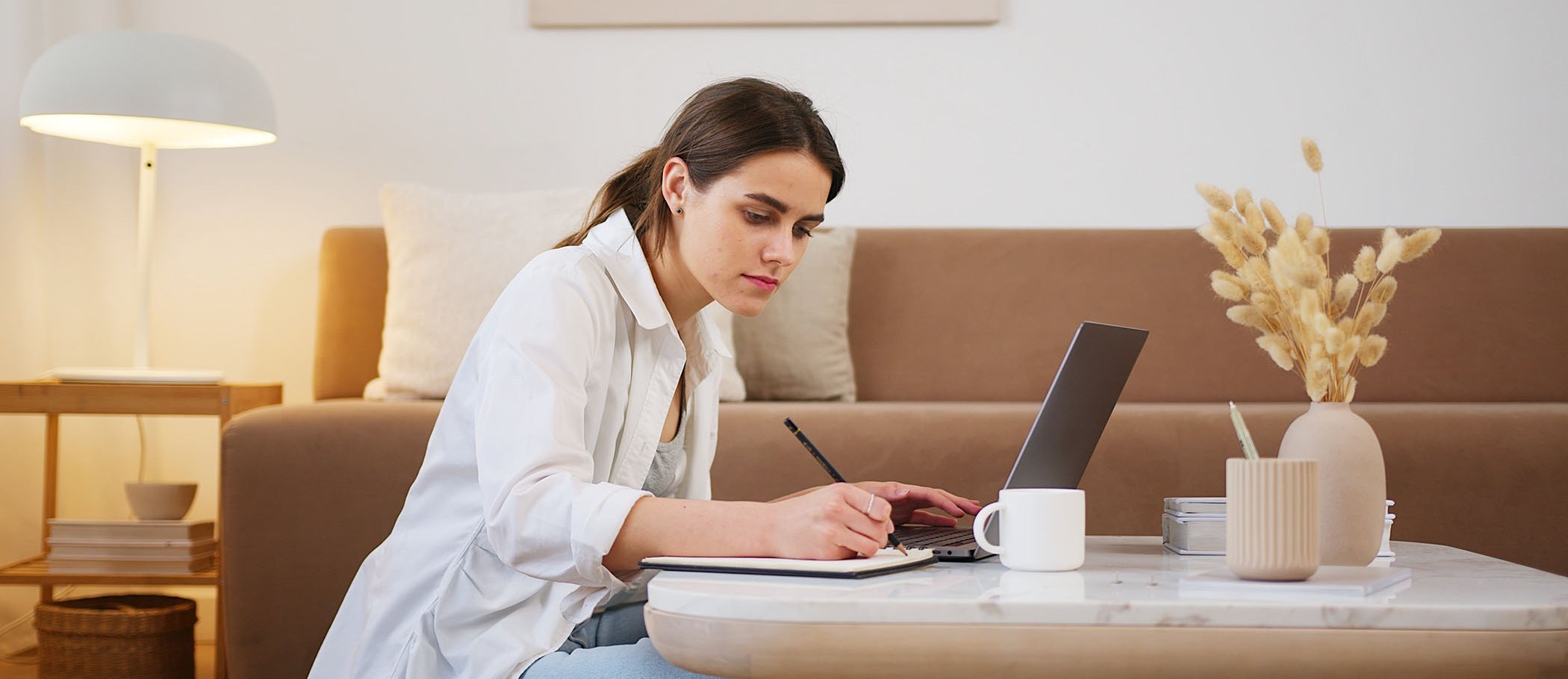 A girl with an open laptop and writing on a notebook