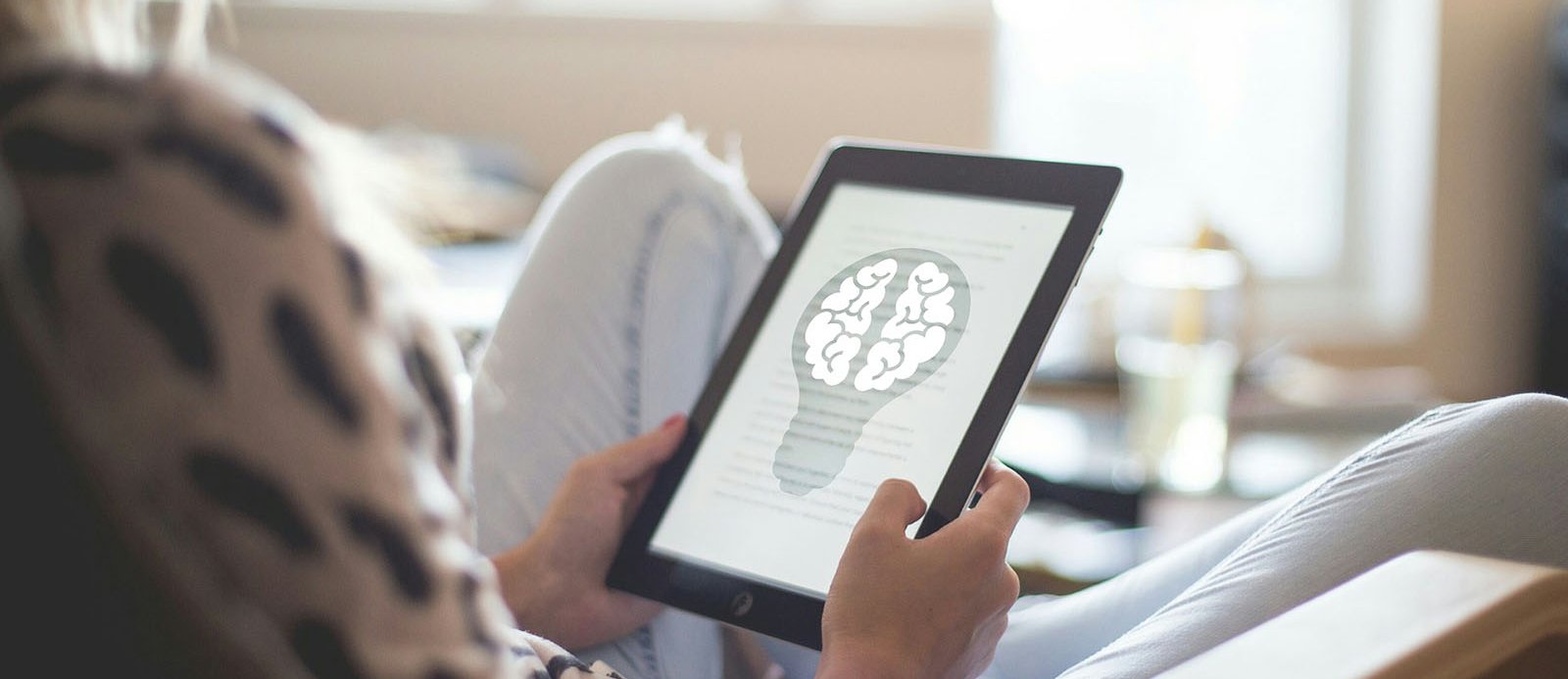 Una persona con un ebook leyendo un texto acompañado de una representación de un cerebro