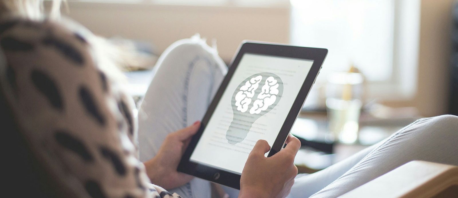 A person with an ebook reading a text accompanied by a representation of a brain