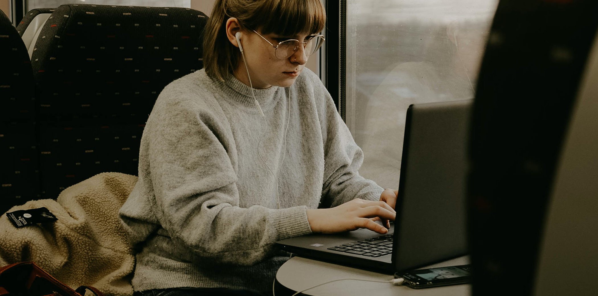 Una noia asseguda en un tren, amb auriculars i escrivint en un portàtil