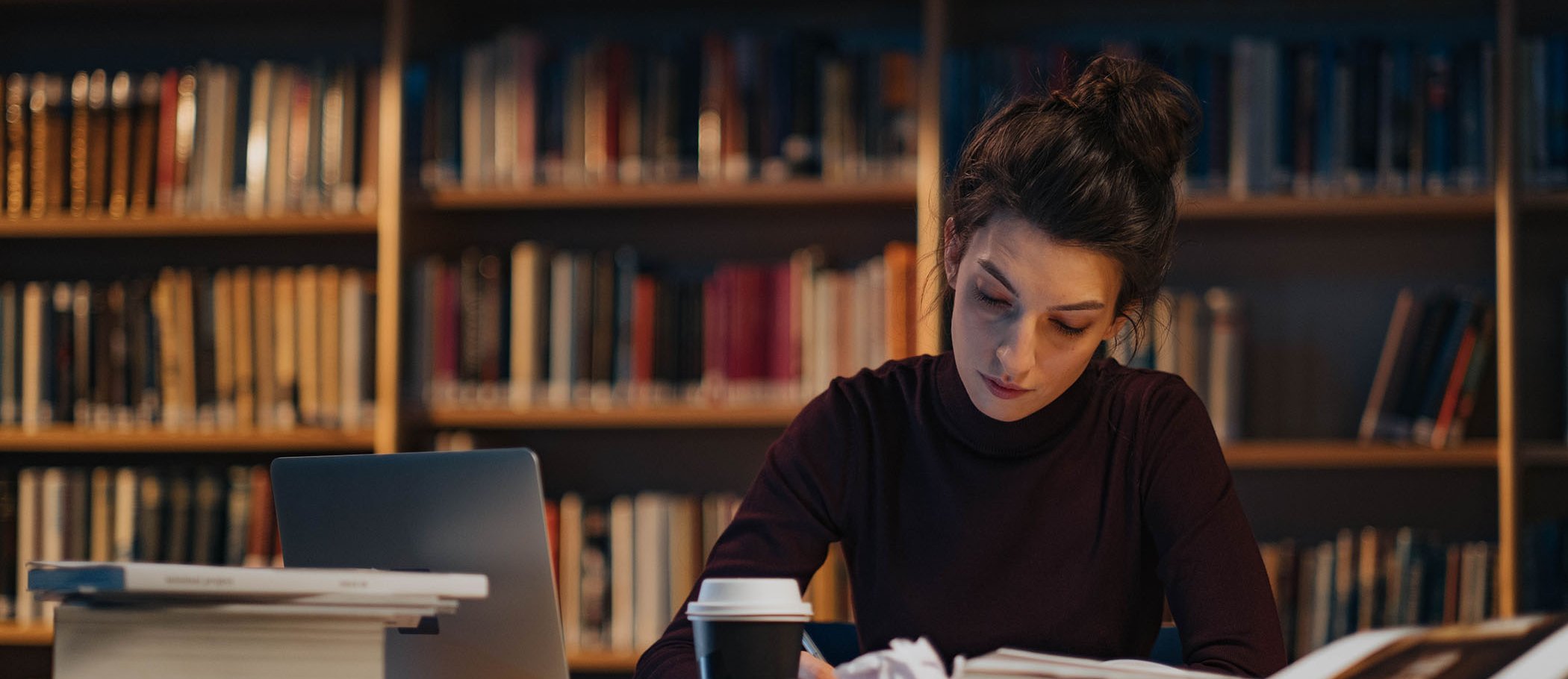 A woman writing on a table full of books and paper sheets