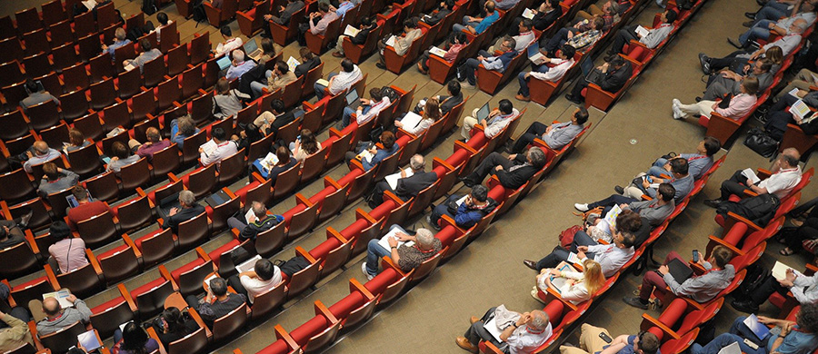Varias personas sentadas en las butacas de un salón de congresos