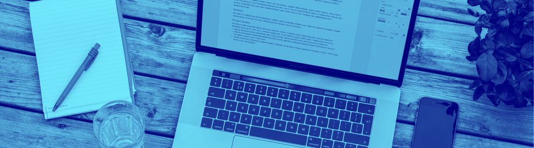 A table with a laptop, a notebook, a pen and a glass of water