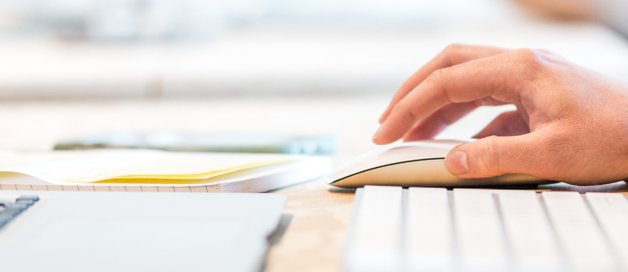 The hand of a person with a mouse and a computer in front of it