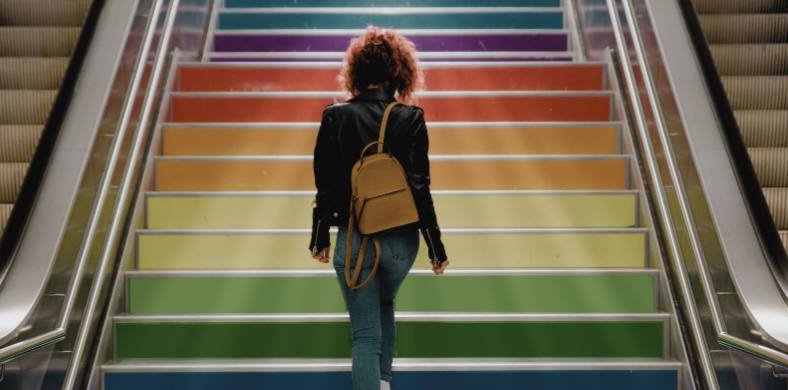 A person climbing a staircase with the colors of the LGBT flag