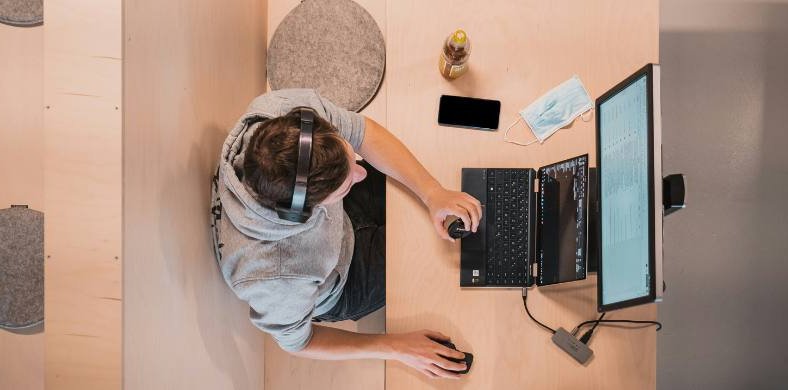 Aerial view of a person with headphones working with a laptop and a screen in a modern space.