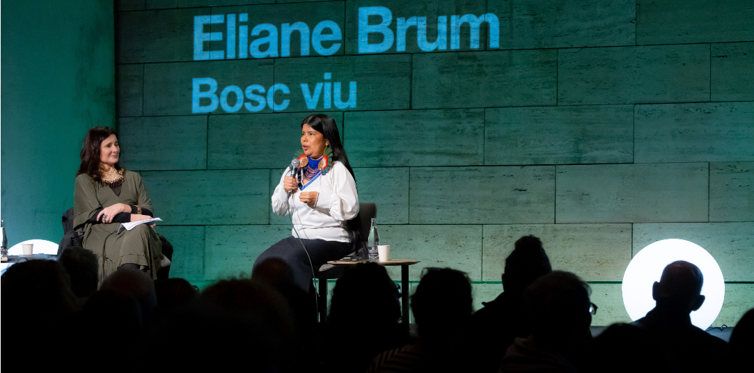 Asistentes del público observan a dos mujeres en una conversación en el escenario del CCCB; una de ellas lleva un tocado grande y colorido.
