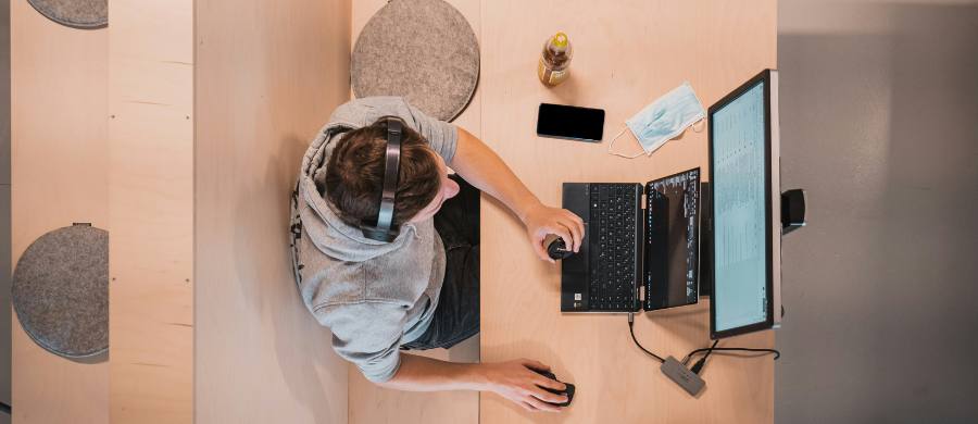 Vista zenital d'una persona amb auriculars treballant amb un portàtil i una pantalla en un espai modern. Vista zenital d'una persona amb auriculars treballant amb un portàtil i una pantalla en un espai modern.