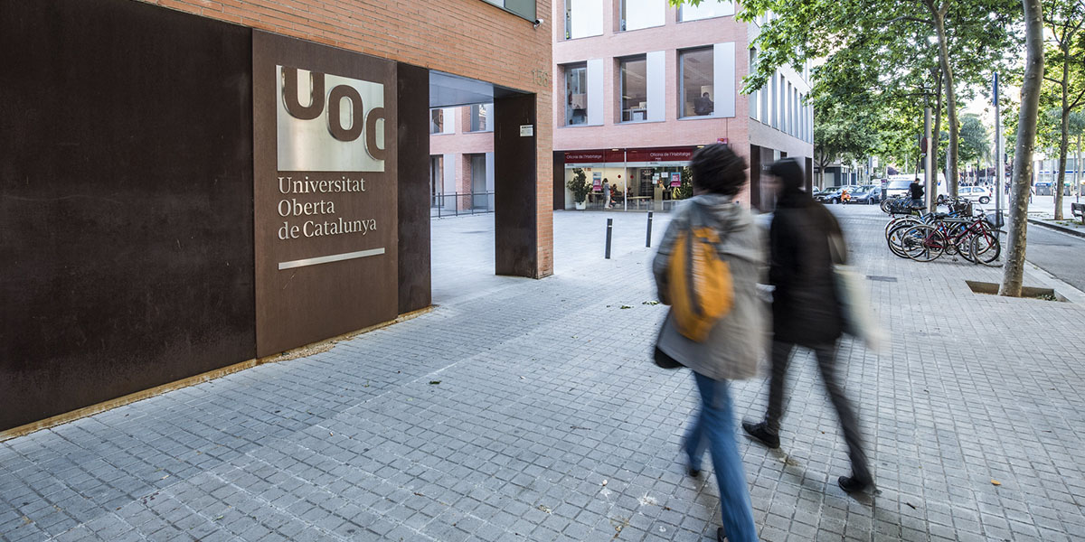 Dues persones caminant cap a un edifici amb el logo de la UOC