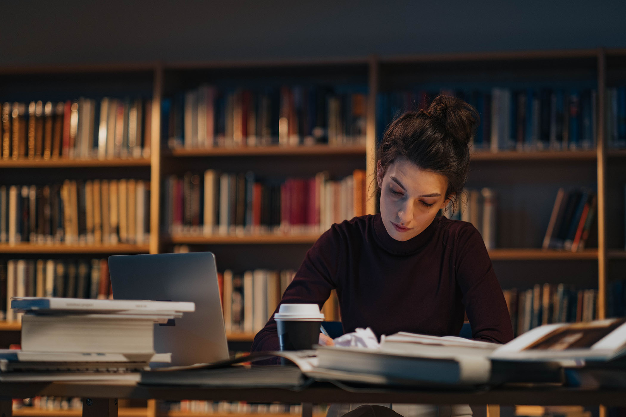 Una dona escrivint a una taula plena de papers i llibres