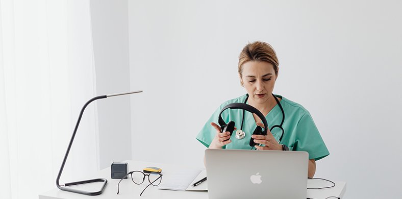 Una mèdica amb un portàtil, auriculars i una llibreta
