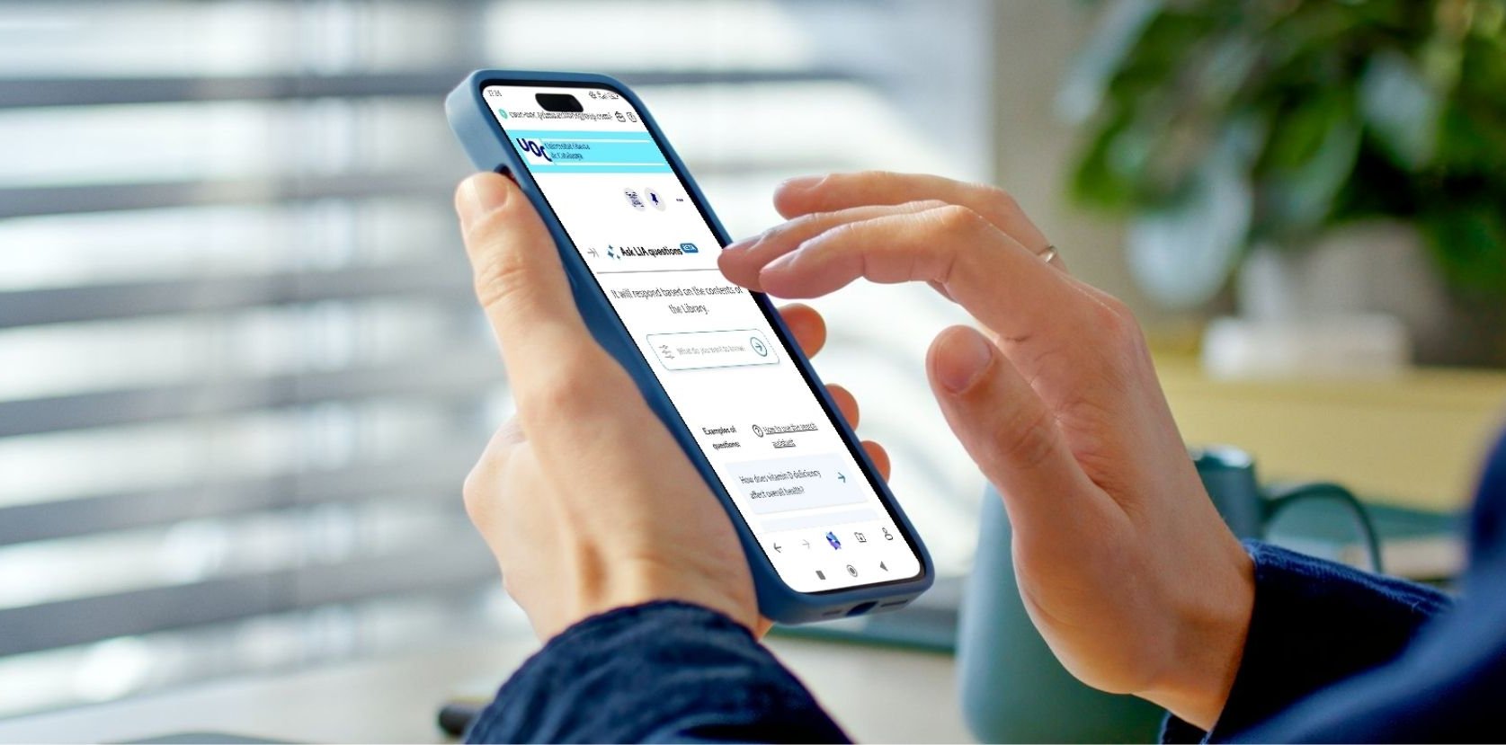 The image shows a person holding a mobile phone with one hand while interacting with the touchscreen with the other. The device displays a webpage featuring the search assistant.