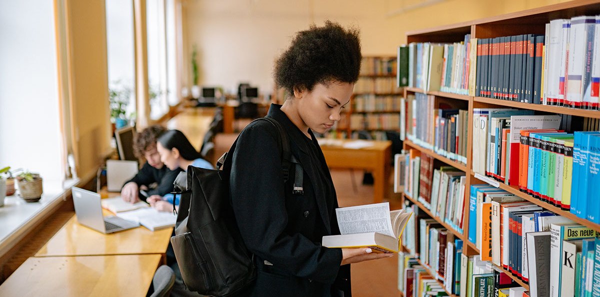 Una persona agafant i fullejant un llibre de la prestatgeria d'una biblioteca