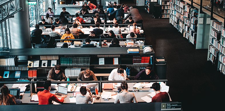 Una secció d'una biblioteca amb taules plenes de persones treballant i estudiant