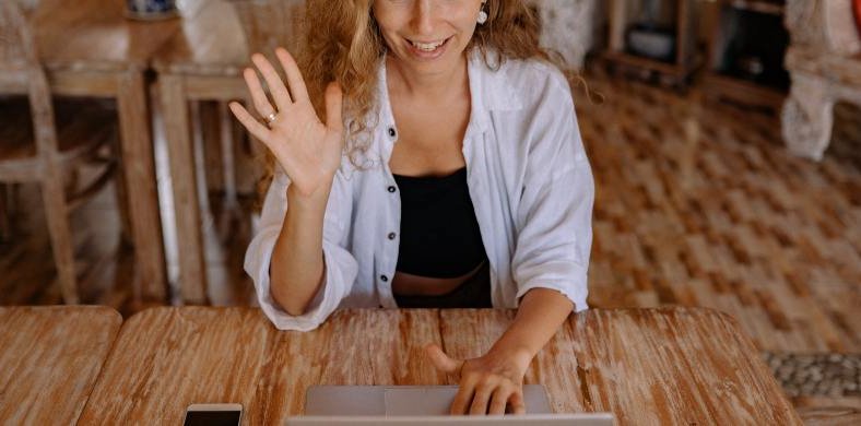 Una mujer saludando delante de una pantalla de ordenador