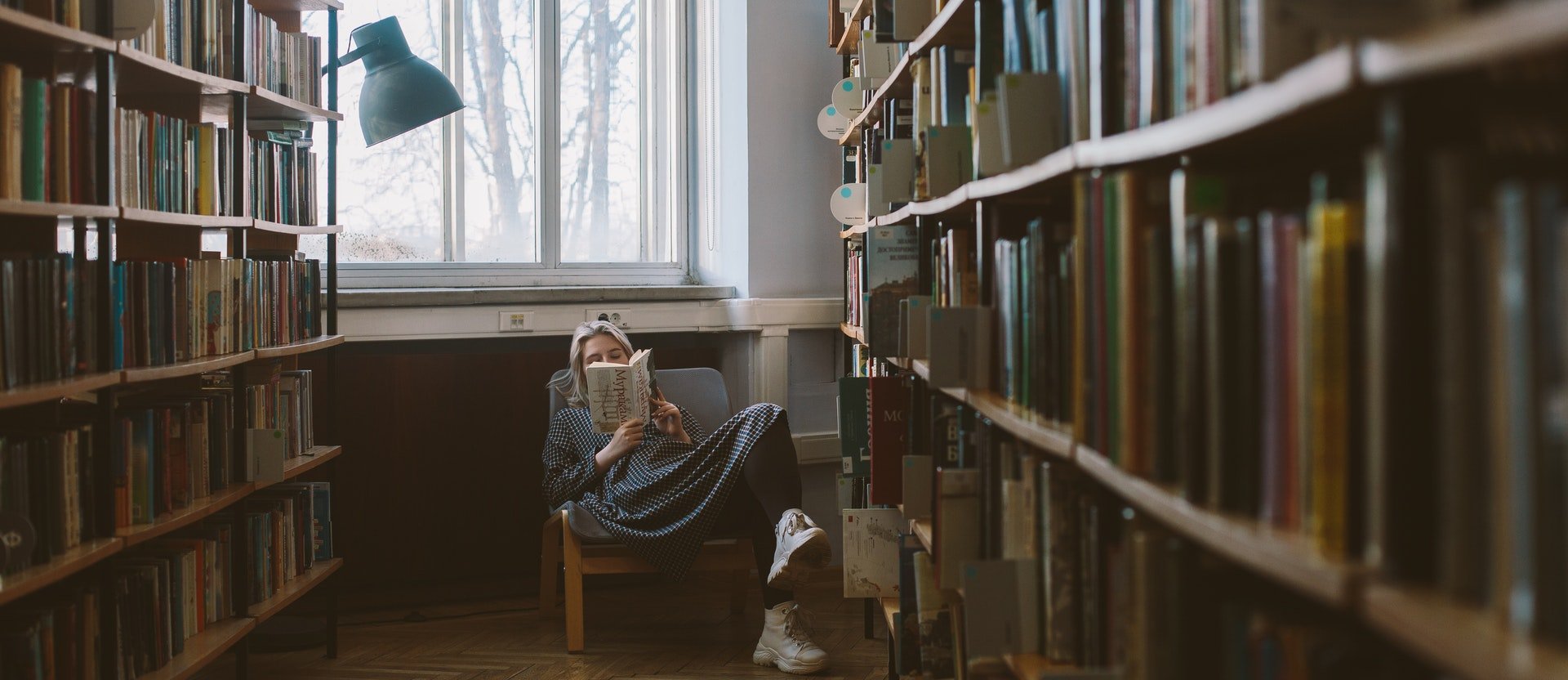 Woman reading a book sitting between shelves