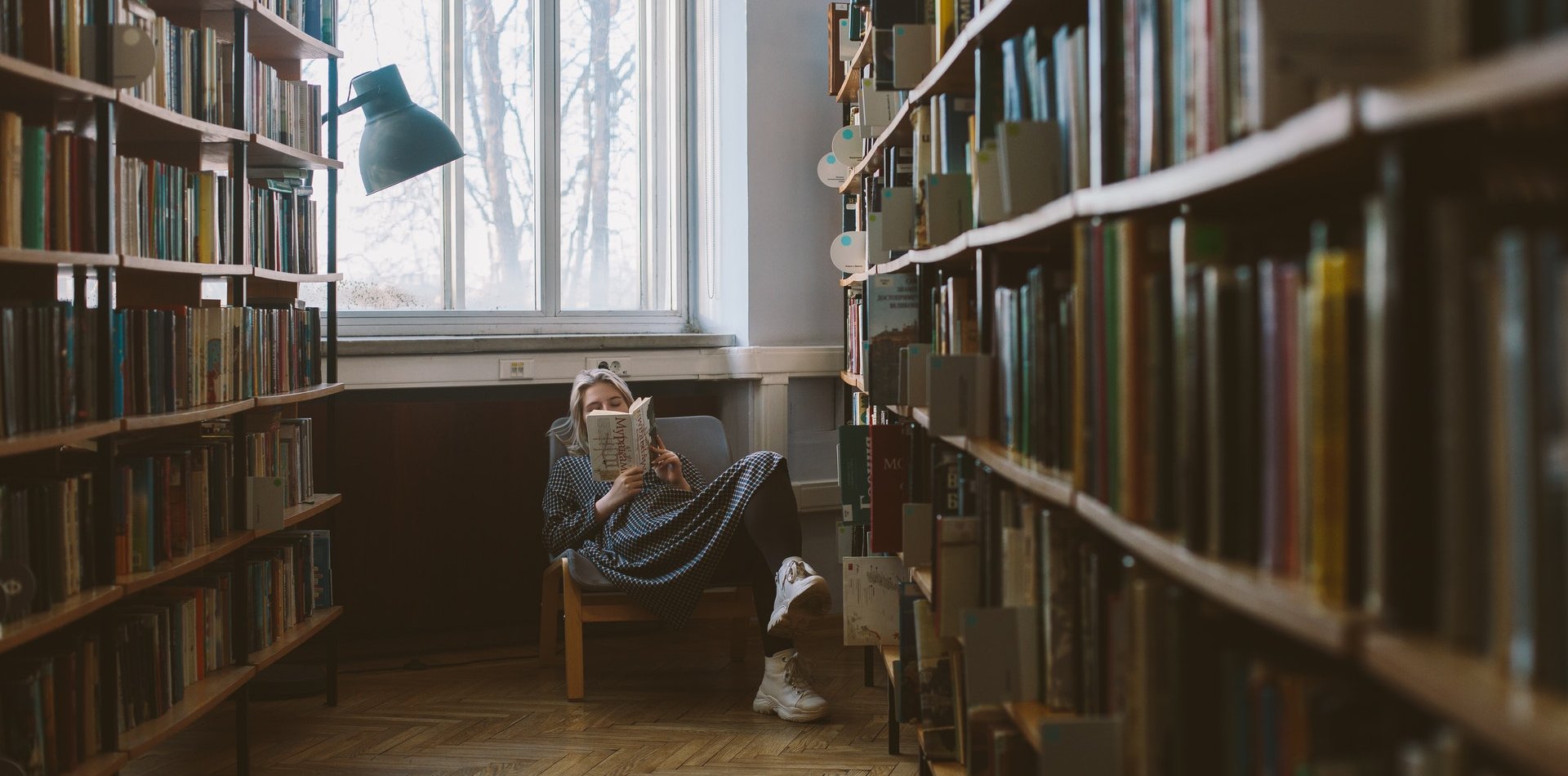 Woman reading a book sitting between shelves