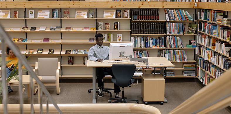 Una persona utilitzant un ordinador al mig d'una biblioteca