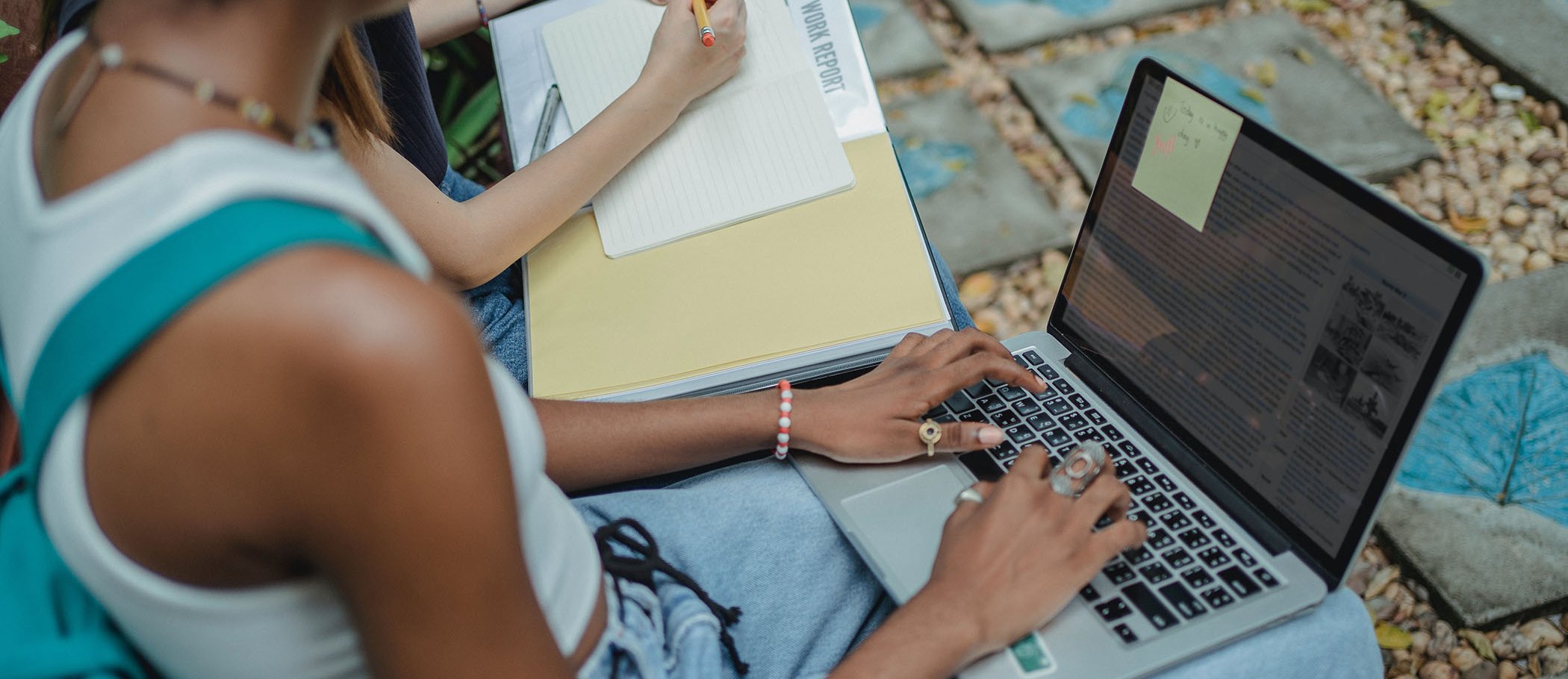 A girl with a laptop and another person taking notes on a sheet