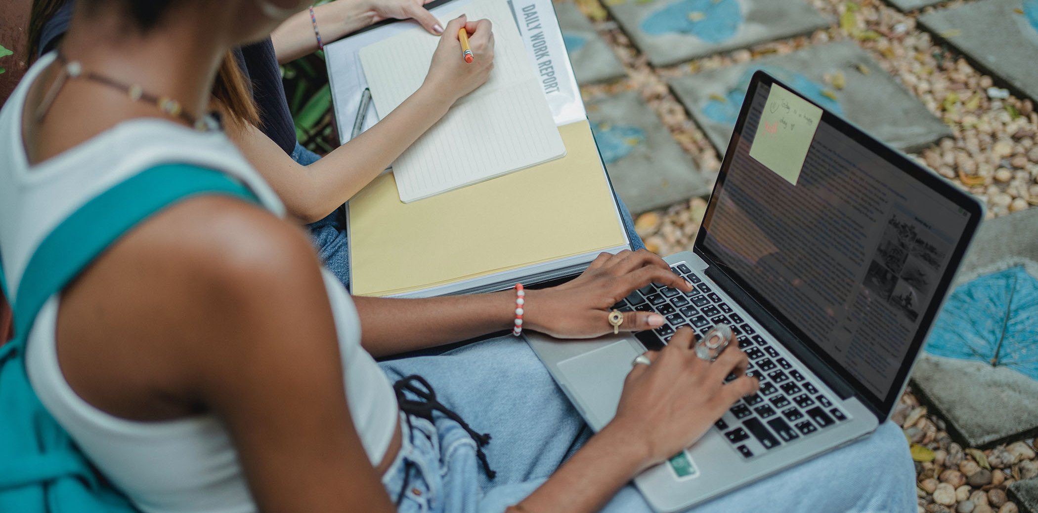 A girl with a laptop and another person taking notes on a sheet