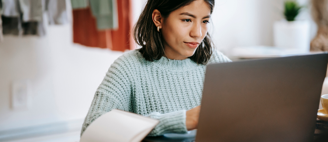 A girl working on the computer and a book next to it